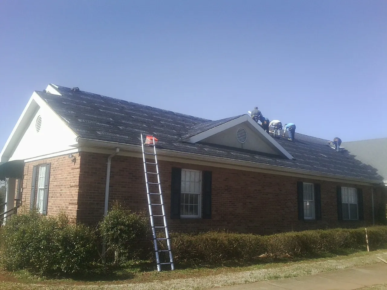 Crew tearing shingles off a brick ranch roof with a ladder set — Emergency Roof Repair work by our crew in Roy