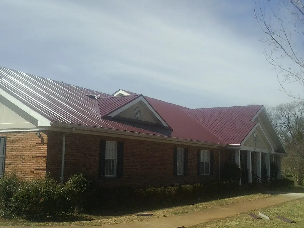 Red metal roof with gabled entries on a long brick building, from a Hail Damage Roof Repair job in Roy
