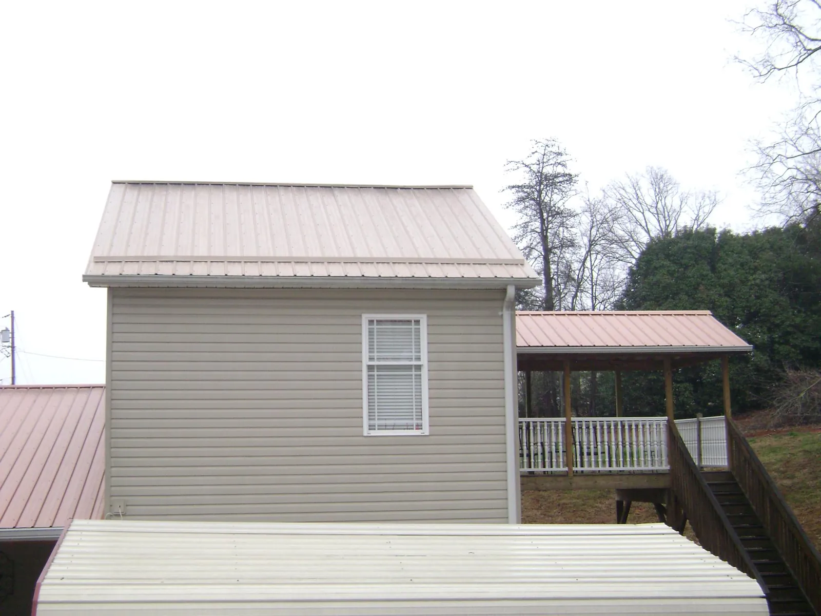 Tan metal roofs on a two story addition and attached porch, from a Roof Replacement job in Roy
